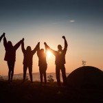 silhouette-of-group-people-have-fun-at-the-top-of-the-mountain-near-the-tent-during-the-sunset